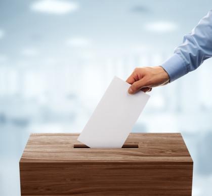 A disembodied hand puts a ballot in a voting box.