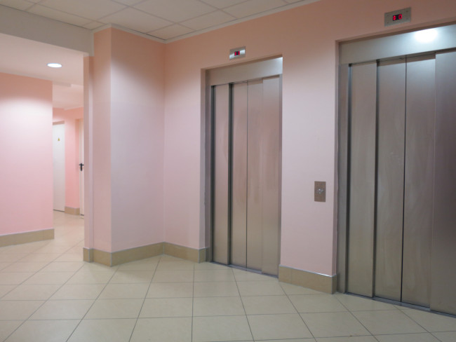 bank of 2 elevators at the base of apartment building lobby with pink walls