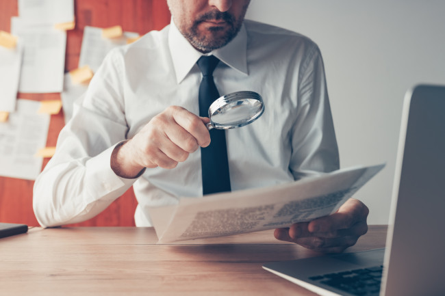 Businessman reading document contract papers with magnifying glass at office desk stock photo