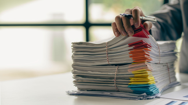 Businessman working in finance with pile of unfinished papers on the desk business paper pile stock photo