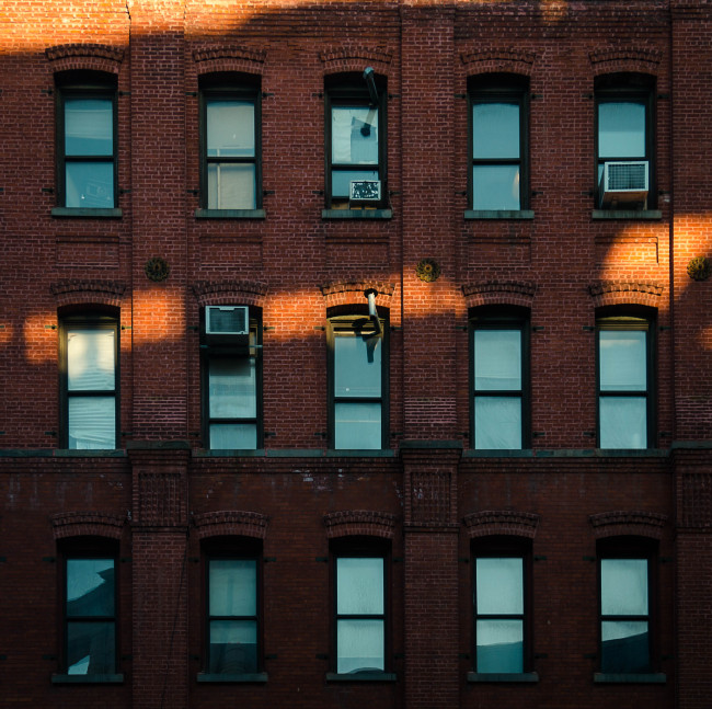 A ray of sunlight hits the red brick facade with blue windows of apartment buildings in New York