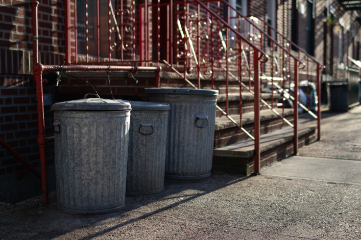 A row of old metal garbage cans outside an urban neighborhood home along a sidewalk in Astoria Queens New York