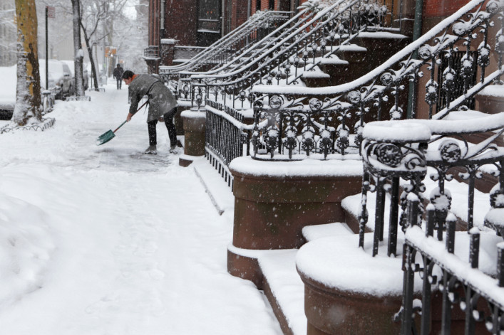 Brooklyn brownstone resident clears snow off sidewalk in winter 