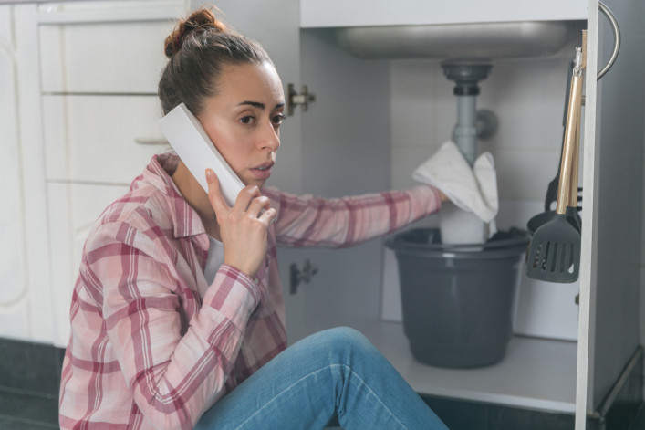 Woman on the phone to a plumber about a leaking sink