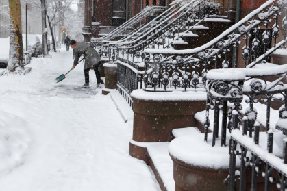 Brooklyn brownstone resident clears snow off sidewalk in winter