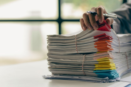 Businessman working in finance with pile of unfinished papers on the desk business paper pile stock photo