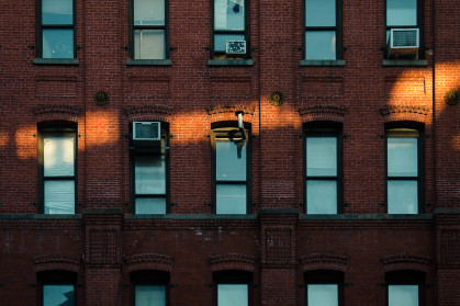 A ray of sunlight hits the red brick facade with blue windows of apartment buildings in New York