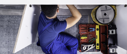 A plumber repairs a pipe beneath a sink