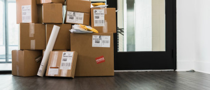 A large stack of cardboard boxes, envelopes and a cylinder are sitting inside a door of a building