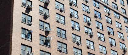 Tall apartment building with air conditioning machine at almost every window in New York city during summer day.