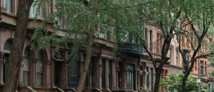 A picturesque view of classic brownstone buildings with lush trees in a serene New York City neighborhood.