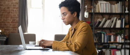 Serious busy young Black laptop user woman working at computer at home office.