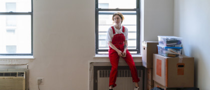 Young woman is sitting on a windowsill in an empty room of a newly rented apartment, tired after moving in. stock photo